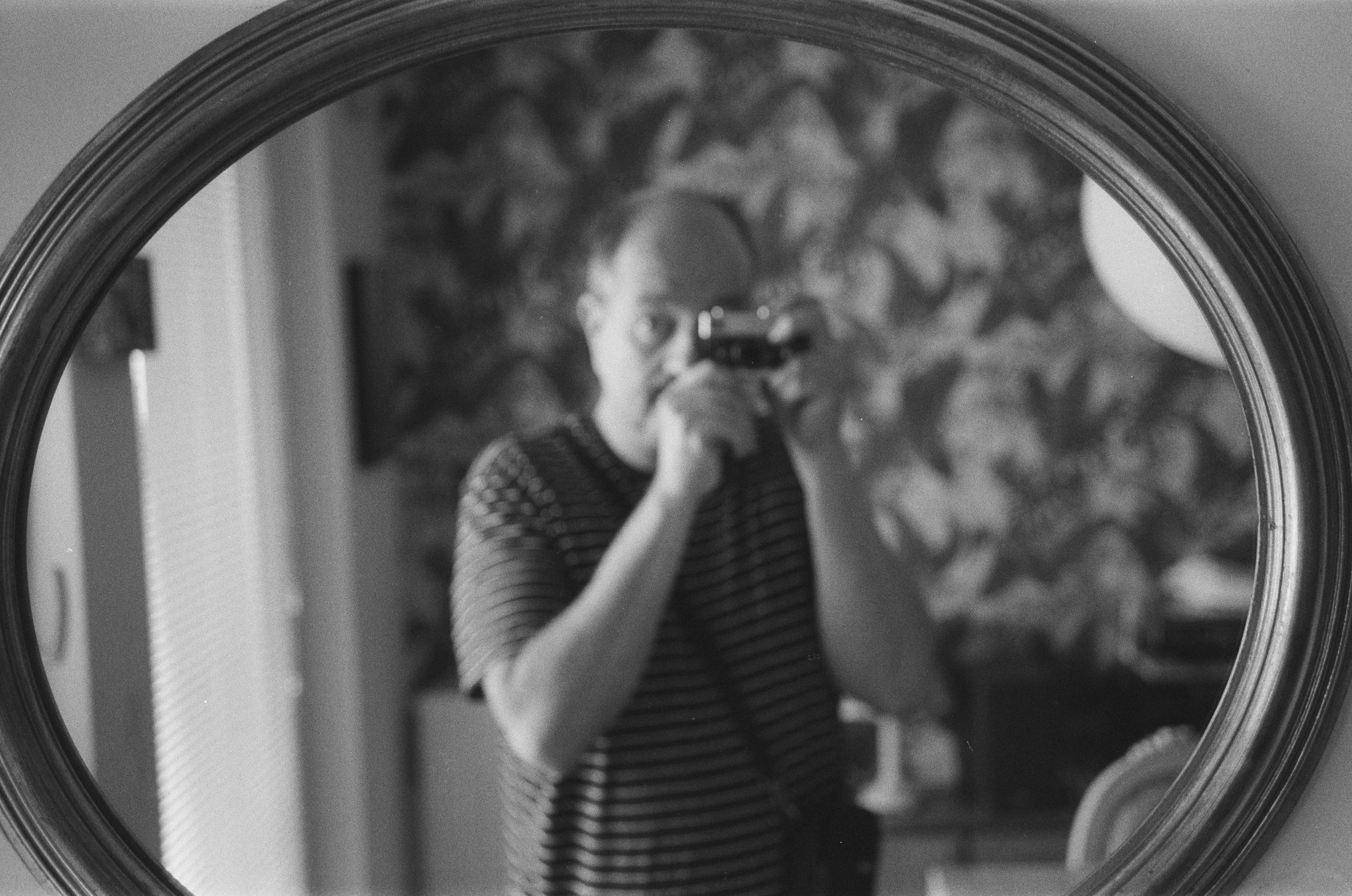 Selfie vor dem Wohnzimmerspiegel. Der Fokus liegt auf dem Rahmen des Spiegels, das Spiegelbild verschwimmt im Death of Field der Sonnar Linse.